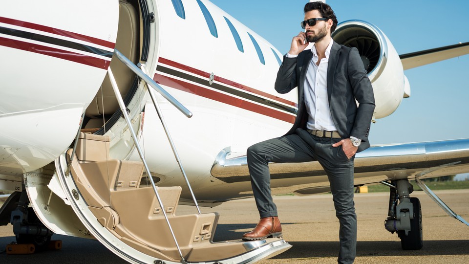 Young businessman with one foot on the staris of a private jet airplane, talking over the mobile phone.